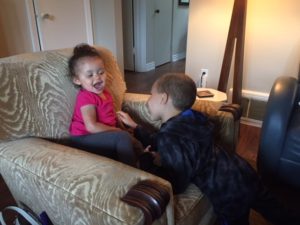Vienna and Ryker very animated as she sits on an upholstered chair and he reaches over to tickle her
