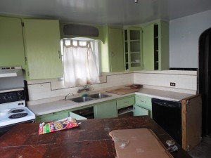 ramshackle, filthy kitchen with doors hanging open and cupboards in two tones of mint green 