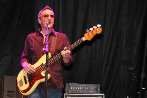 dark-haired Peter Fredette, wearing a maroon suit, playing guitar and singing on stage