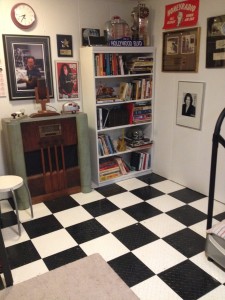 black and white checked floor with no drums. Bookshelf, antique radio and posters are visible