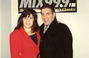 I have long and slightly unruly hair, wearing a red jacket arm in arm with a smiling Pat Harrington under a MIX 999 banner