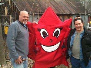 Kevin, 6-foot-4 and bald, wearing a grey jacket and jeans, and Derek - 5-foot-9 wearing a black jacket with his sunglasses on his head, flank what looks like a giant red star with a huge happy face on it.