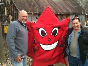 Kevin, 6-foot-4 and bald, wearing a grey jacket and jeans, and Derek - 5-foot-9 wearing a black jacket with his sunglasses on his head, flank what looks like a giant red star with a huge happy face on it. 