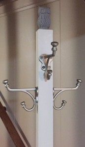 cream-coloured coat rack with small, soft-grey owl on top. Silver coat hooks on all four sides.