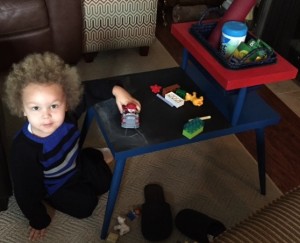 Ryker sits next to his new table and plays with a truck. Chalk is laid out on the chalkboard top.
