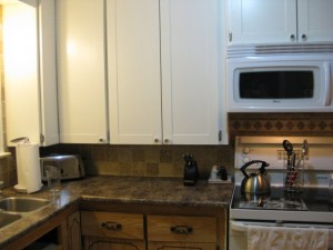 A photo of the new, white shaker-style cupboards on top with the old, dingy wood cupboards below the new granite-look countertop