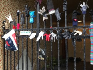 iron railing with dozens of mismatched gloves attached and a sign that reads Single Gloves Speed Dating