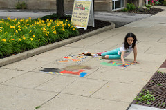little girl drawing pictures including a rainbow on a sidewalk