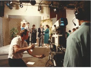 Shot of the riser with me and a few others toasting with champagne, with the backs of a camera man and director in the foreground