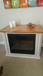 finished fireplace surround done in a creamy beige with a varnished barnboard mantle.