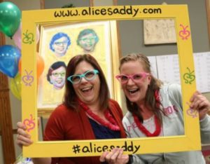 Pal Lianne and I holding up a picture frame with Alice Saddy contact info on it, wearing big, bright sunglasses