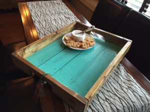 Varnished tray with bare wood edges and a lightly distressed light blue surface. Has brie and crackers on a plate on it.