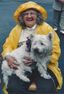 Auntie B in a bright yellow rain slicker and rain hat holding Wee Mac who's wearing a purple corsage on his collar