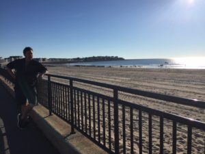 Derek leans against a railing overlooking the beach at sunset