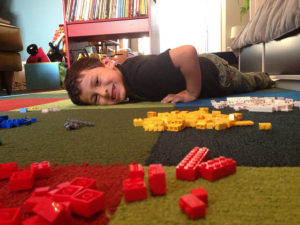 Boy lying on the carpet amid piles of lego pieces, smiling at the camera