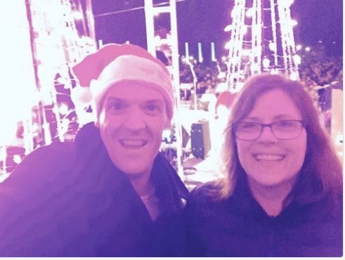 selfie of me and Ken with the backs of the performers behind us, as we stood backstage waiting to go on. I have a tiny santa hat clipped to the side of my head.