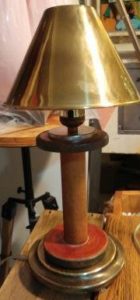 old, wooden sewing machine bobbin about 8 inches tall is now a lamp with a brass shade