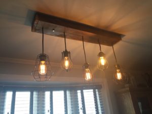 Barnboard base on the ceiling with five pendants suspended at slightly different lengths, each with a metal cage and an Edison bulb