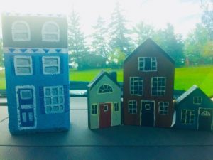 Victorian-style house front painted on a brick. Three small wooden houses with peaked roofs, attached by hinges.