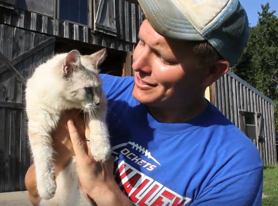 Destin Sandlin holding and looking at a white cat as they get ready to learn