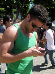 Young man in a green muscle shirt looking down at his phone as he texts