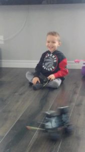 Ryker sitting on the floor with a huge smile on his face while the remote-controlled Jeep passes him in a blur
