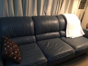 blue-grey couch with a brown/cream cushion on it and a cream throw