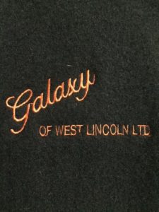 Close-up of the embroidered company name in orange on the front of a black wool jacket