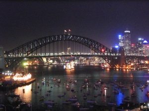 nighttime view of Sydney Harbour with hundreds of boats in the foreground and purple and gold lights on a bridge and along the shorelines