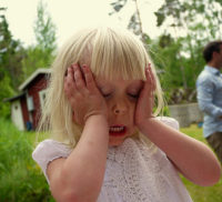 Little girl outside on a summer day holding her head in her hands and screaming in frustration