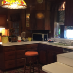 The kitchen features an orange and brown colour scheme with a tiffany lamp, white laminate counter-tops and dark wood cabinets. The floor is carpeted in orange and brown. It's roomy.