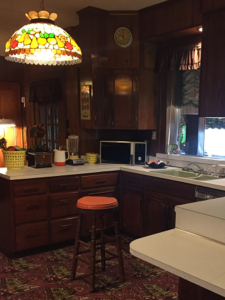 The kitchen features an orange and brown colour scheme with a tiffany lamp, white laminate counter-tops and dark wood cabinets. The floor is carpeted in orange and brown. It's roomy.