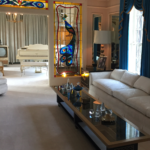 This room is all done in shades of white. The custom-made glass-top coffee table runs the length of a huge, white couch. A white grand piano sits past stained glass windows of navy blue and yellow