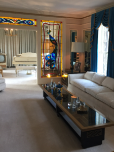 This room is all done in shades of white. The custom-made glass-top coffee table runs the length of a huge, white couch. A white grand piano sits past stained glass windows of navy blue and yellow