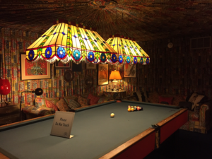 Two large Tiffany lamps over a huge pool table. The ceiling and walls are covered in pleated fabric of rust, yellow, green and gold.