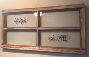 wood-framed, four-pane window with "Life begins" in script in the upper left pane and "with coffee!" in the lower right pane. Coffee is in capital letters. 