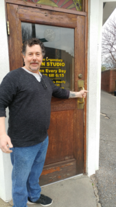 Derek opening the door to a humble little building with yellow lettering that reads Sun Studio and the hours of operation.