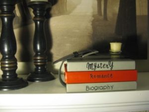 books stacked beside wooden candlesticks, titled Mystery, Romance, Biography