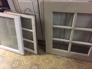 Three old windows of varying sizes leaning against a cabinet. Flooring is a wild, busy pattern in brown and yellow. 