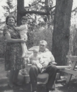 Black and white photo of our grandparents holding us. It's outside beside a big tree. Grandma is holding me - I'm about 2 years old. Kevin is on Papa's lap. He's an infant.