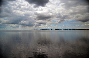 view across clear blue water with blue sky peeking out behind fluffy white clouds