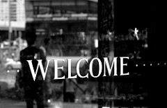 Welcome in right lettering with a dark shop window behind it 
