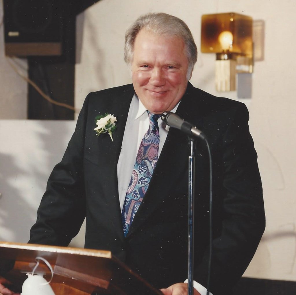 My Dad in 1993, at the podium making a speech at my wedding, looking healthy and smiling wearing a dark suit and a yellow carnation on his lapel