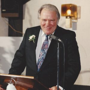 My Dad in 1993, at the podium making a speech at my wedding, looking healthy and smiling wearing a dark suit and a yellow carnation on his lapel