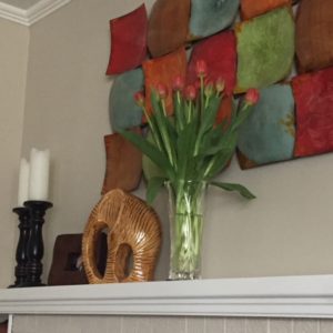 vase full of red tulips on a white fireplace mantle, beside a yellow ceramic elephant, framed picture of me and my brother and two large wooden candlesticks with white pillar candles