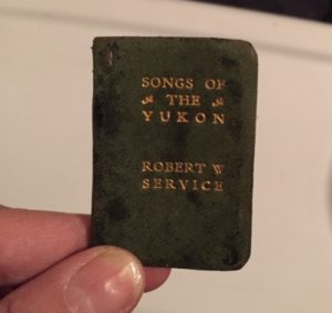 A two-inch-by one-inch book with a green, suede cover titled Songs of the Yukon, Robert W. Service