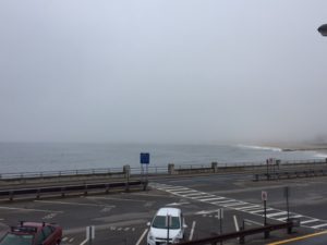 rough waves coming in to shore. The view is from a second floor balcony and overlooks a parking area before the water