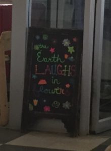 Sandwich board sign reads The earth laughs in flowers.