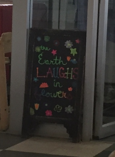 Sandwich board sign reads The earth laughs in flowers. 