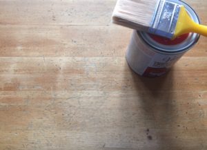part of the pine table shows more wear. Can of top-coat and a brush sit beside it